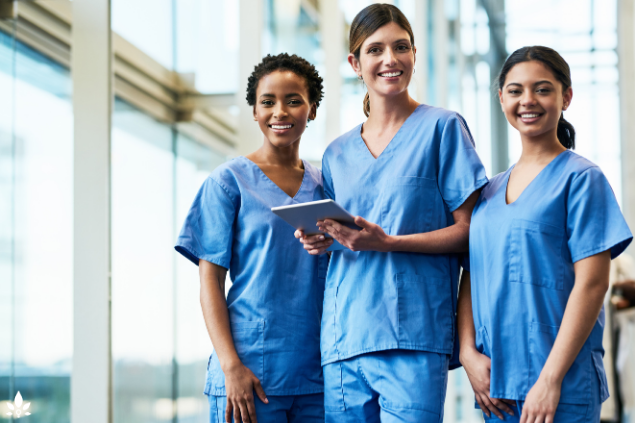 Three women in scrub suits smiling and holding a tablet, promoting lower medical costs for women.