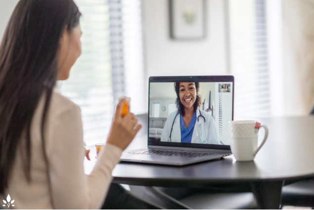 A woman sitting at a table with a laptop and a cup of coffee, discussing benefits of telehealth services at workplace in the Middle East.